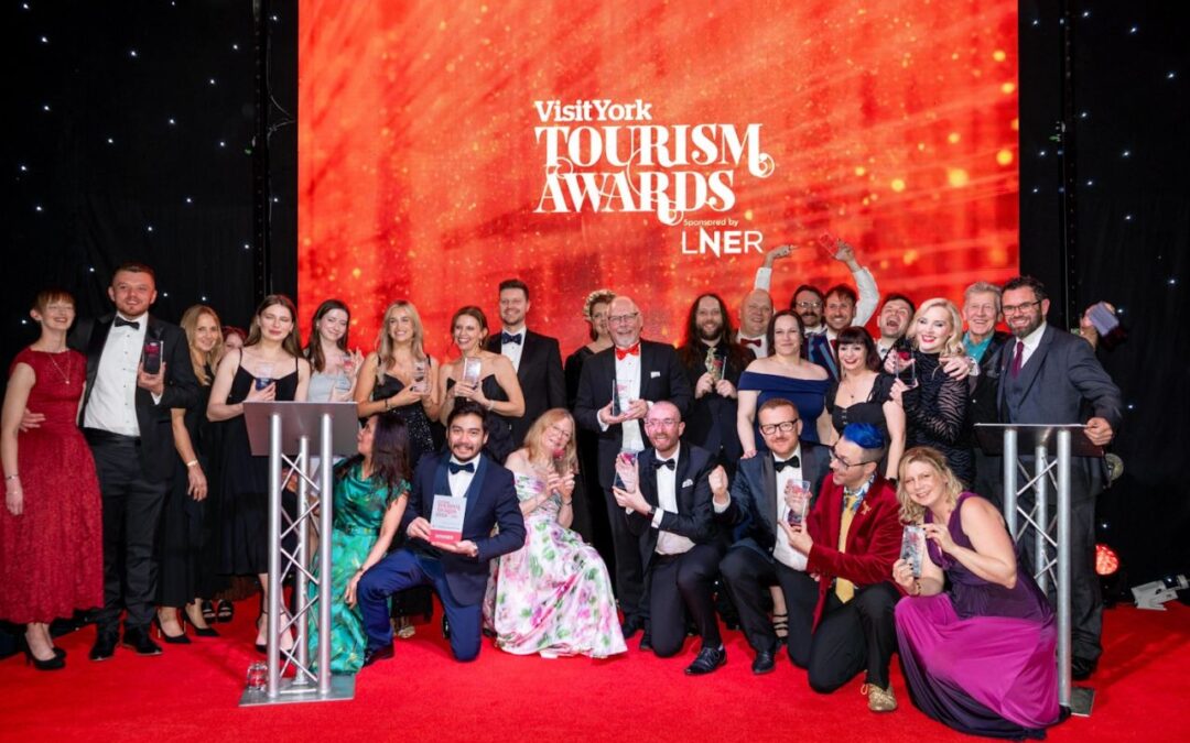 A group of people dressed in formal wear next to a podium and a backdrop which says Visit York Tourism Awards