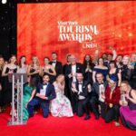 A group of people dressed in formal wear next to a podium and a backdrop which says Visit York Tourism Awards