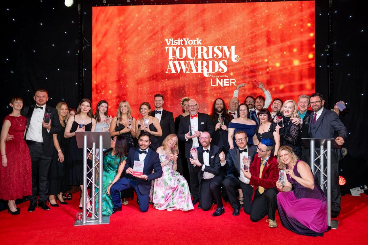 A group of people dressed in formal wear next to a podium and a backdrop which says Visit York Tourism Awards