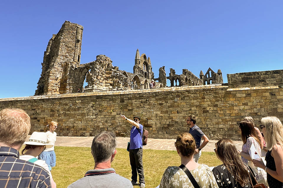 Whitby Tour Guide A group stand in front of Whitby Abbey on North Yorkshire while a knowledgeable expert describes the gothic history of the site.